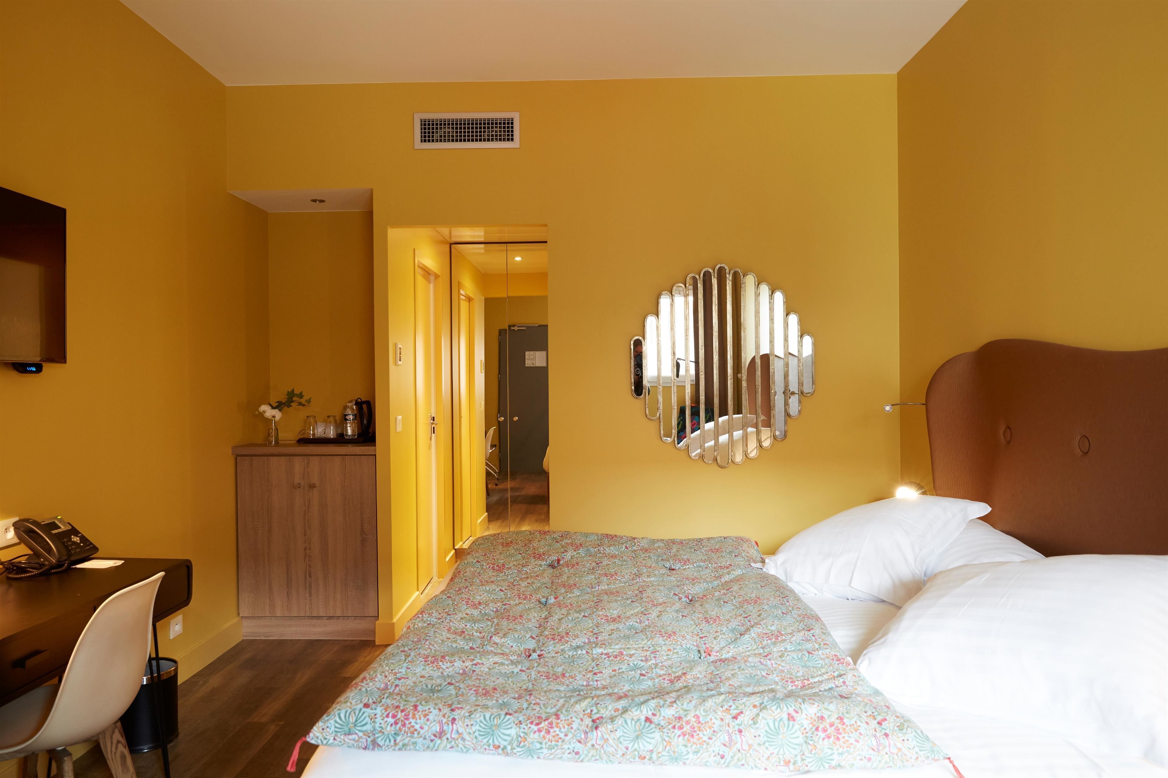 Una habitación de hotel con cama, escritorio con teléfono, espejo y armario.