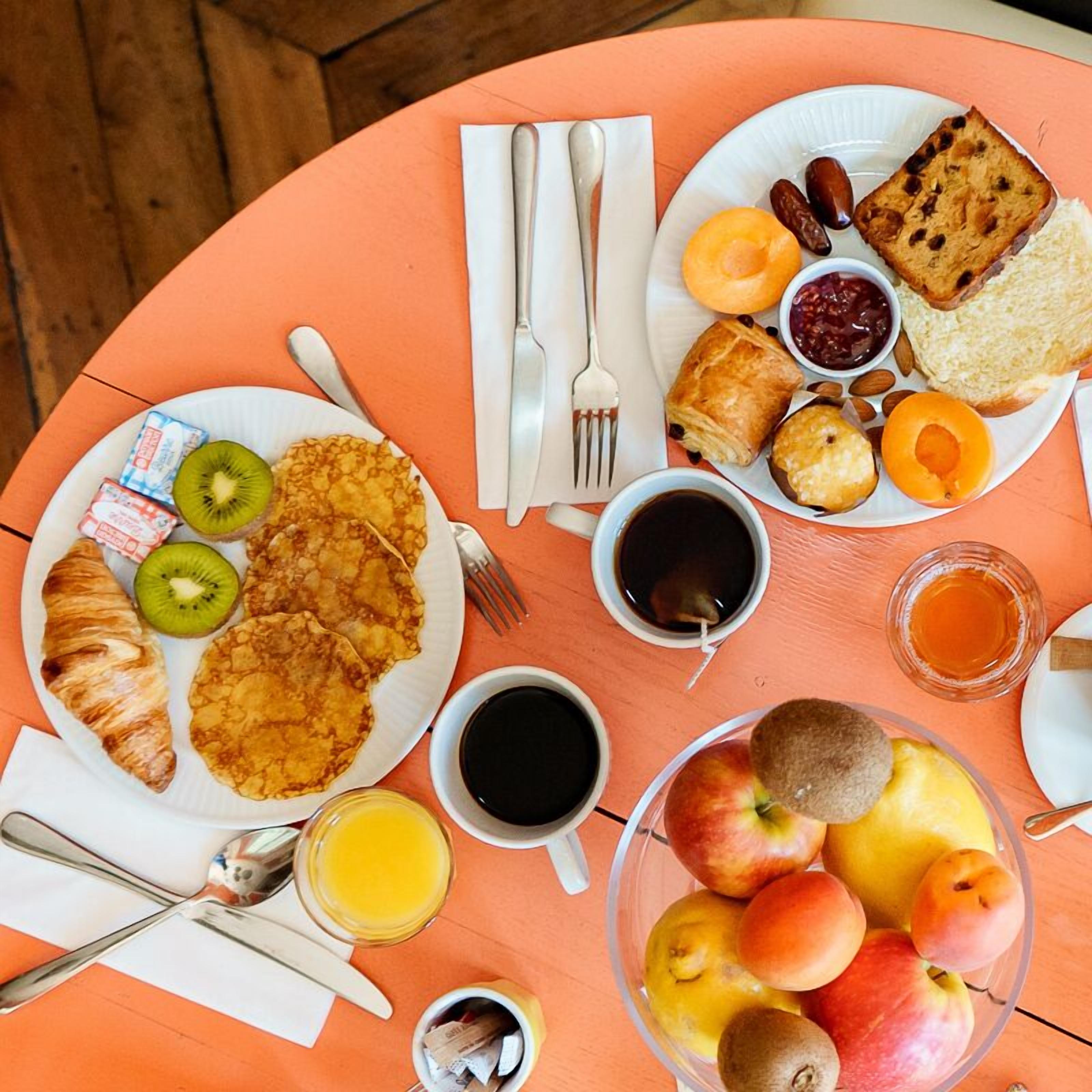 Ett frukostbord med tallrikar fyllda med mat, koppar med dryck och en skål med frukt.
