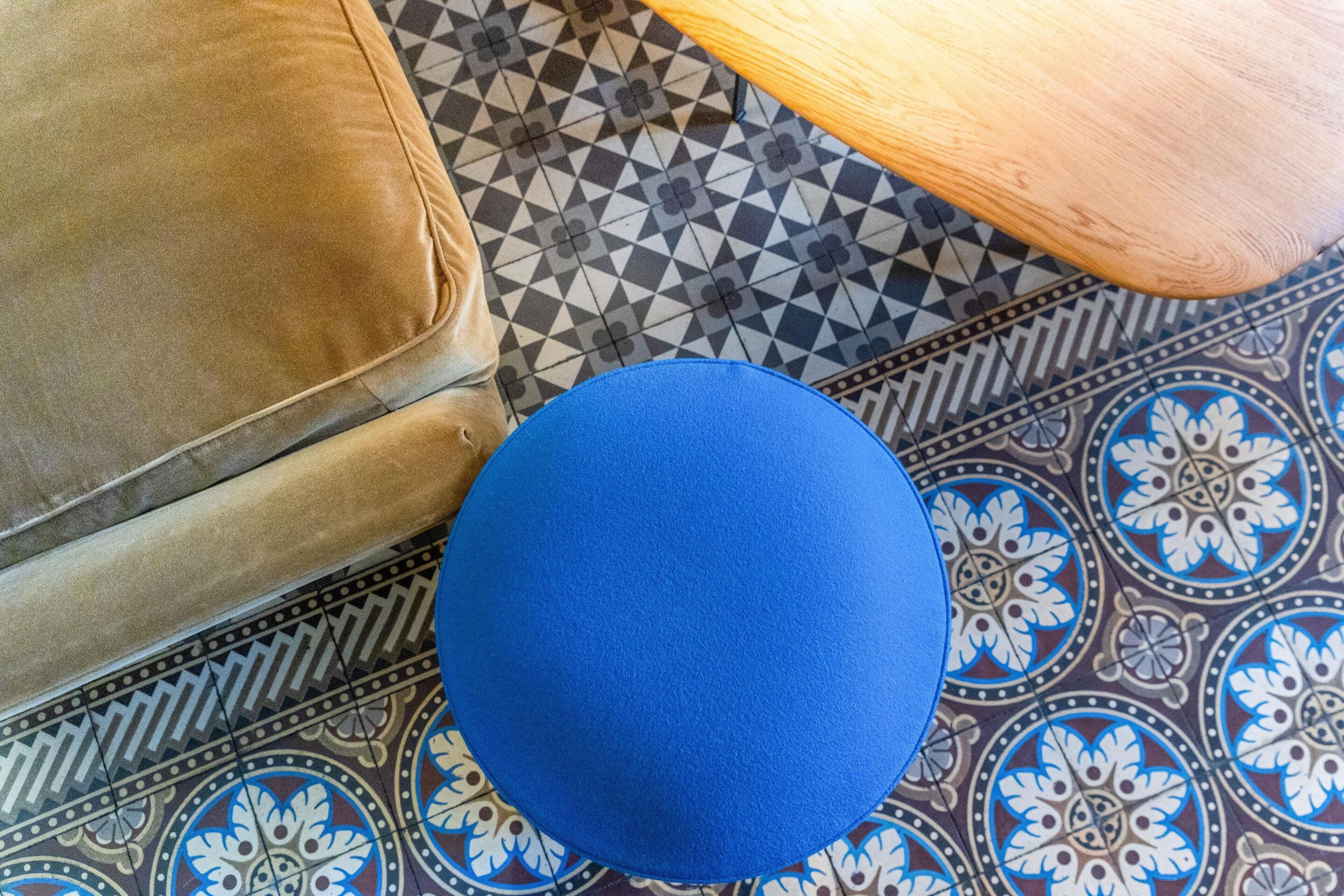 Un taburete azul sobre un piso estampado, con un sofá marrón y una mesa de madera.