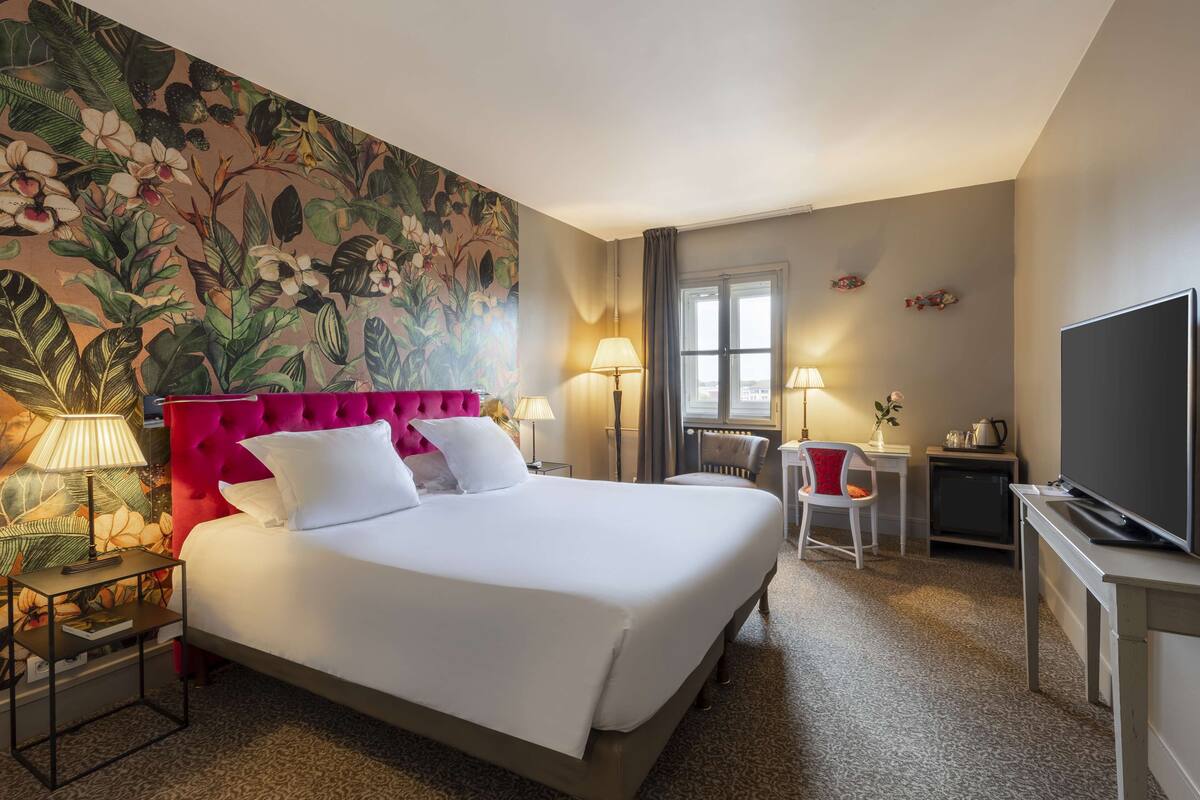 A hotel room with a large bed, a television, a desk, and a chair.