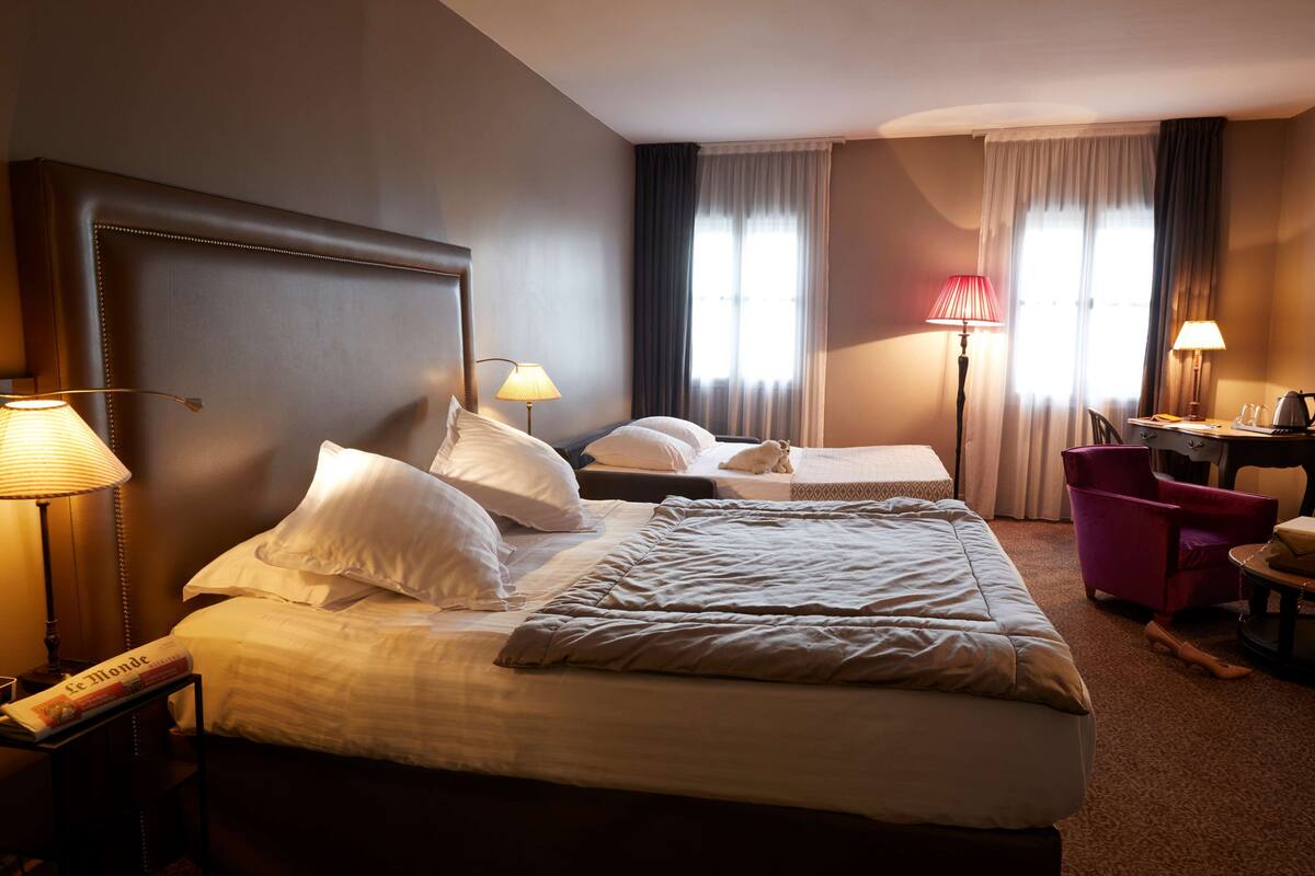 A hotel room with a large bed, two bedside tables with lamps, a desk with a chair, and a window with curtains.