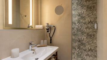 Une salle de bain avec un lavabo blanc, un miroir, un porte-serviettes et un espace douche orné de carreaux à motifs floraux.