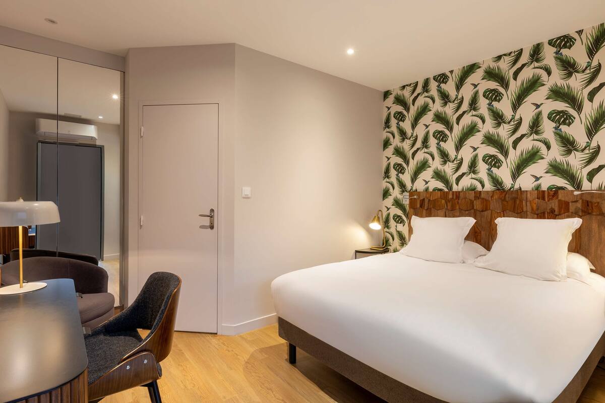 A modern hotel room with a large bed, a desk with a chair, and a glass partition wall.