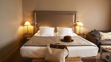 A hotel room with a large bed, two bedside tables with lamps, a brown leather sofa, and a patterned rug.