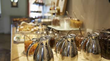 A kitchen counter with multiple stainless steel coffee pots and various food items in the background.