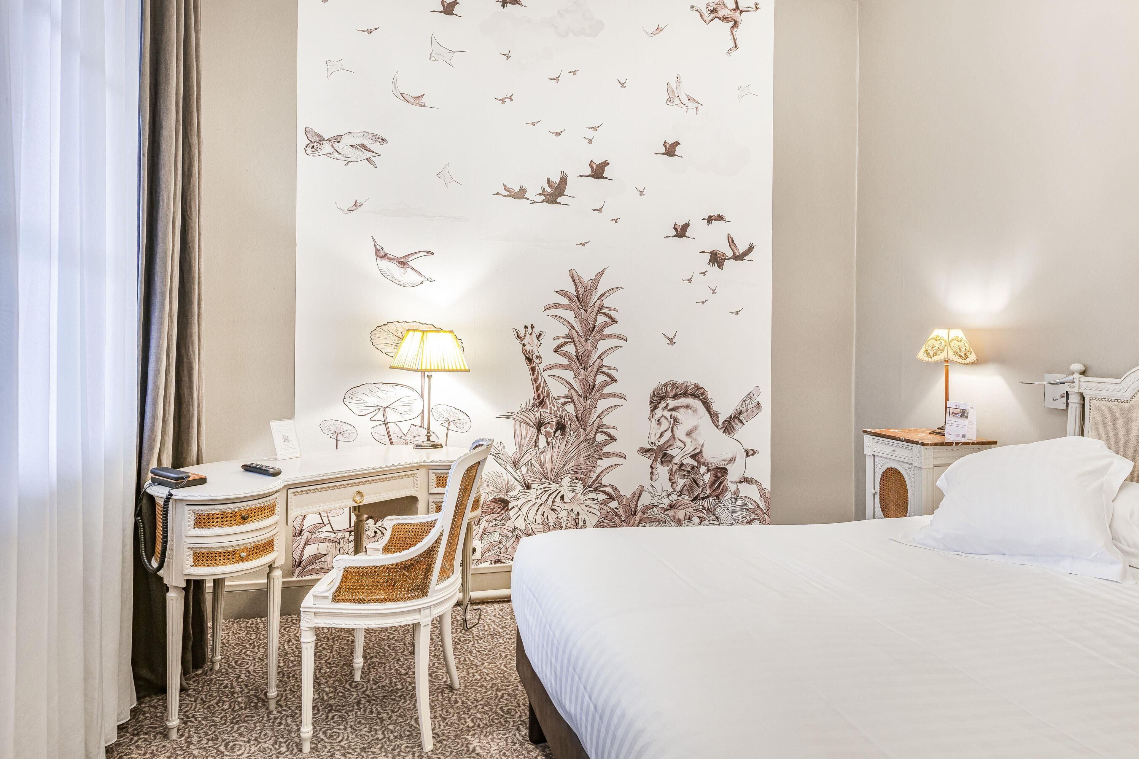 Habitación de hotel con cama, escritorio, silla, lámpara y un mural en la pared.