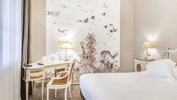 Habitación de hotel con cama, escritorio, silla, lámpara y un mural en la pared.