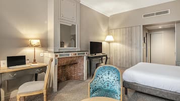 A hotel room with a bed, desk, chair, TV, and a fireplace.