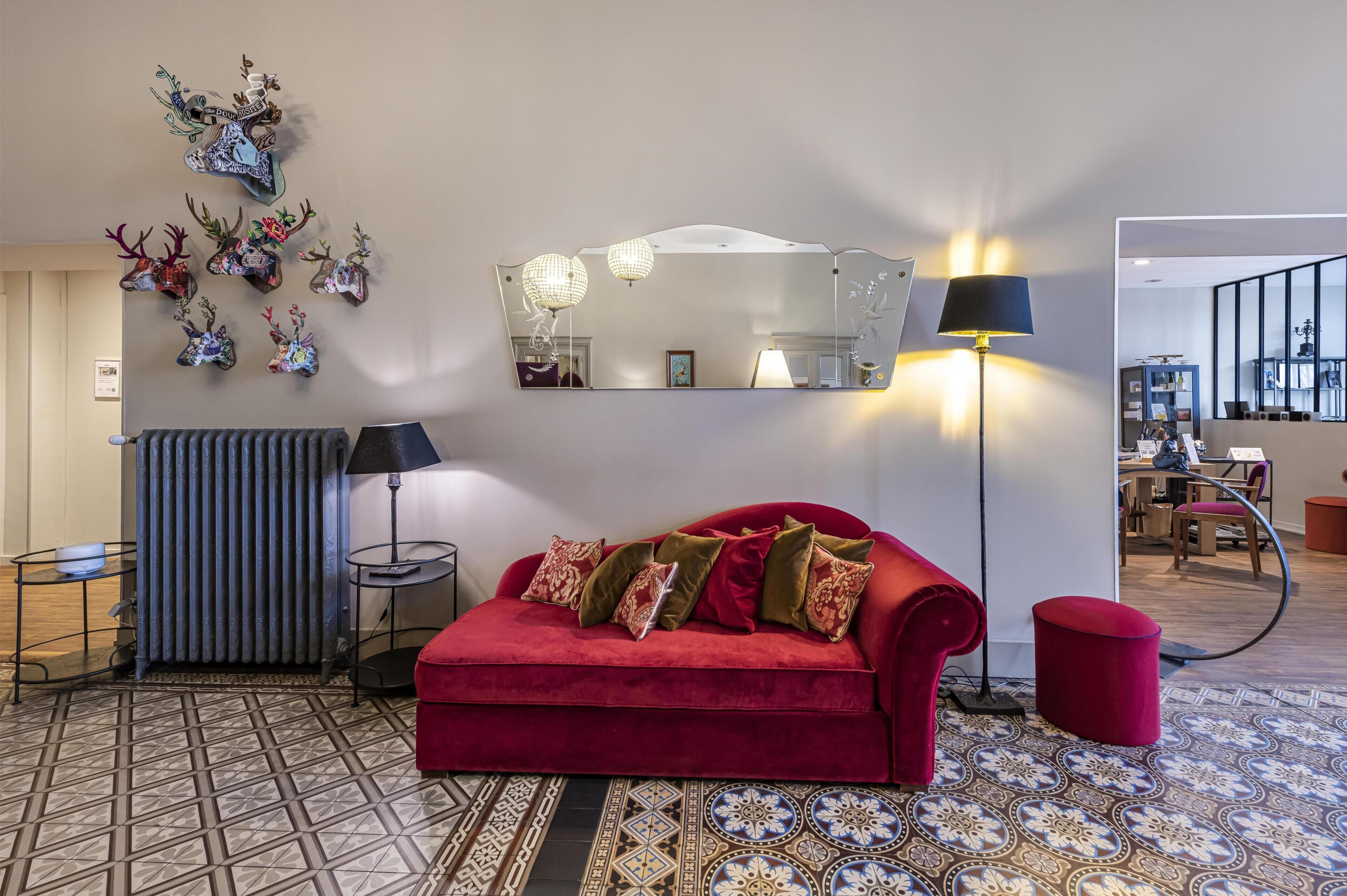 A red sofa with patterned cushions, a large mirror, decorative deer wall art, a floor lamp, and a patterned rug.