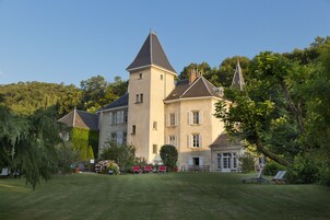 Suuri, historiallinen rakennus, jossa on huomiota herättävä torni ja useita ikkunoita. Rakennuksen ympärillä on vehreää kasvillisuutta ja hyvin hoidettu nurmikko.