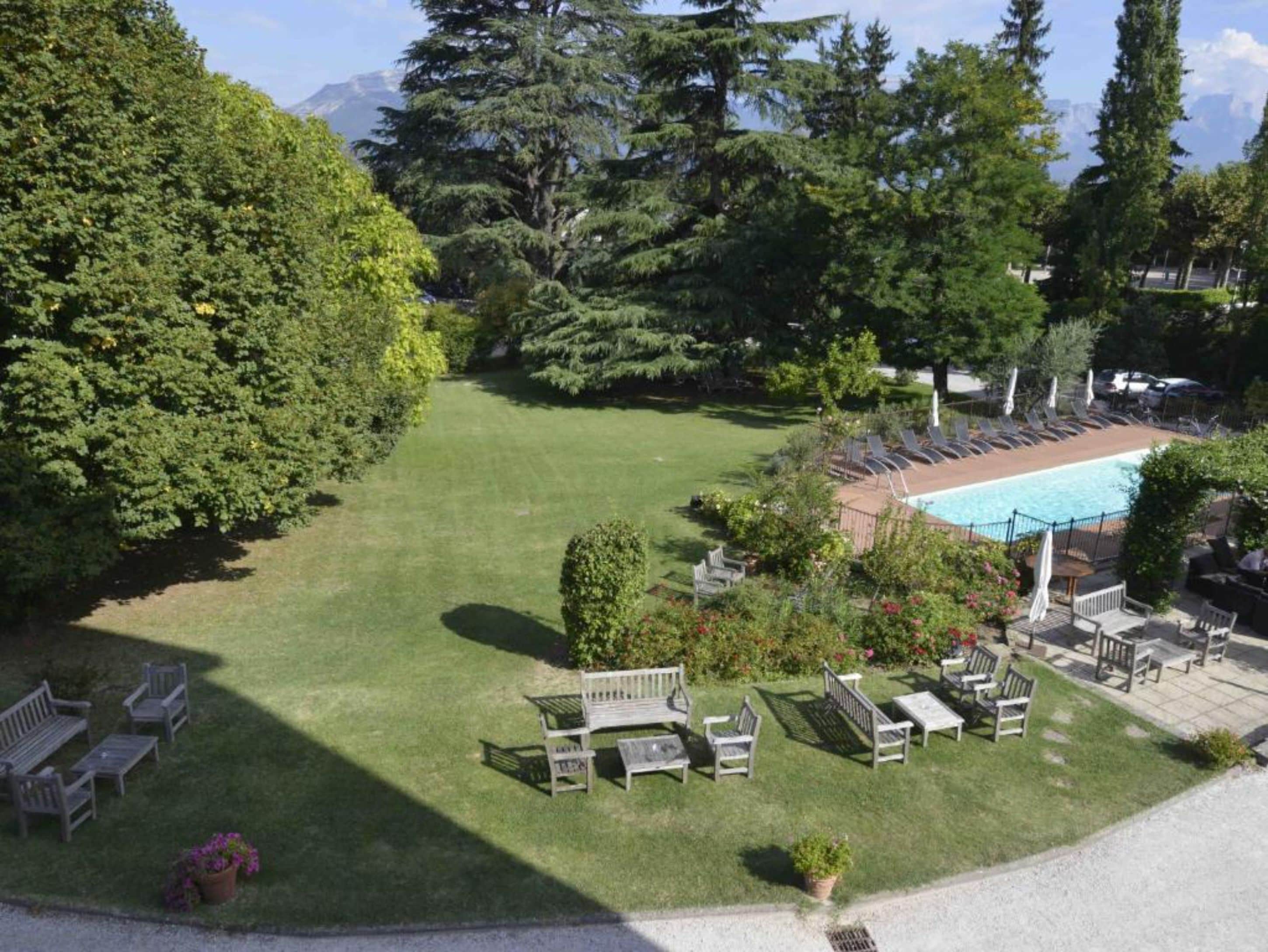 Zona de piscina con sillones reclinables y un pequeño jardín con bancos.