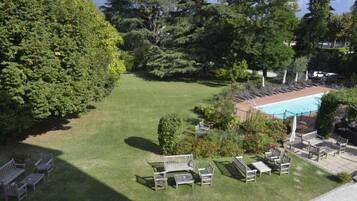 Zona de piscina con sillones reclinables y un pequeño jardín con bancos.