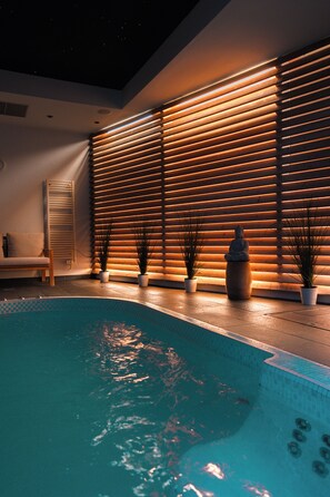 A modern indoor pool area with a wooden slatted wall, a statue, and potted plants. - Château & Spa de la Commanderie (Eybens)