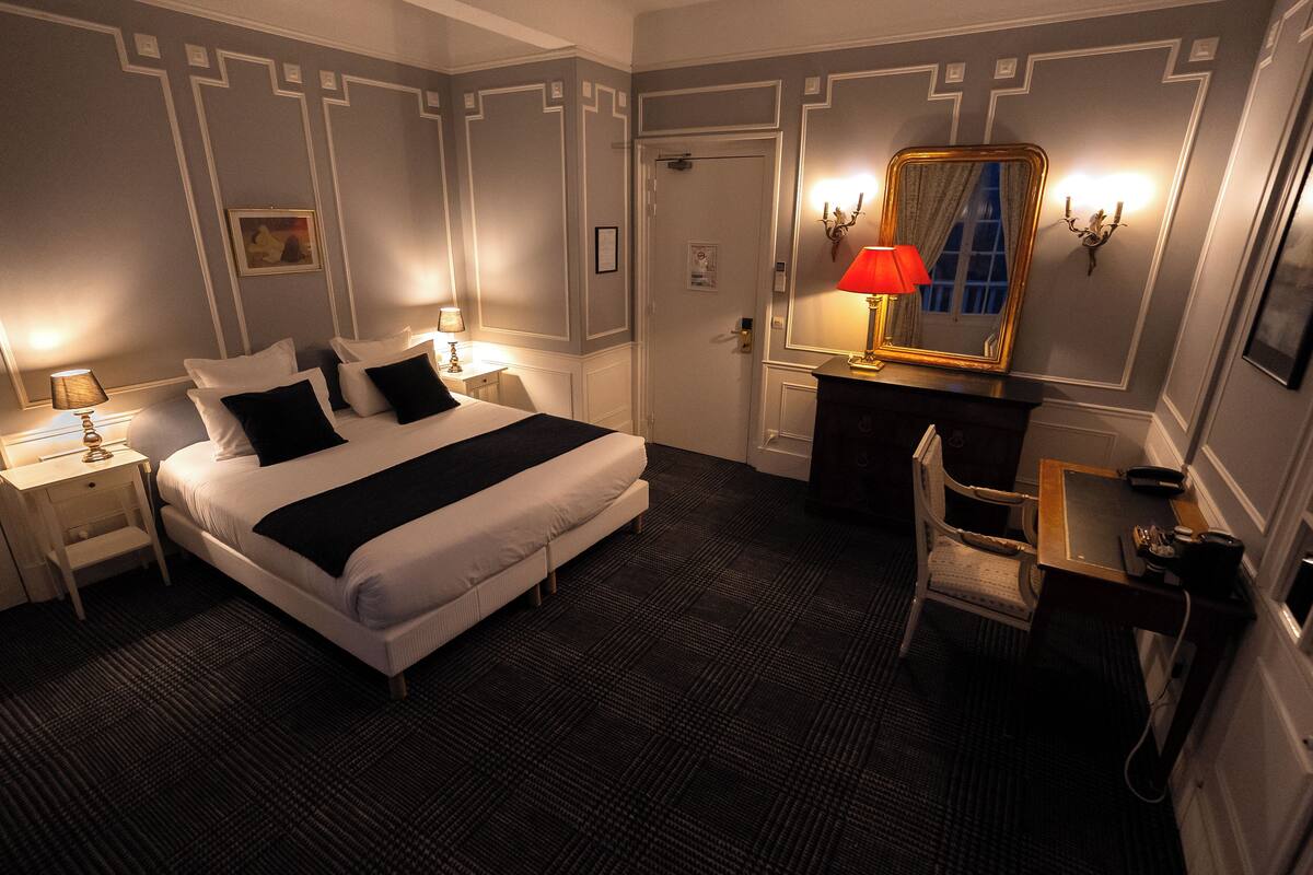 A hotel room with a large bed, a desk, a chair, and a mirror.