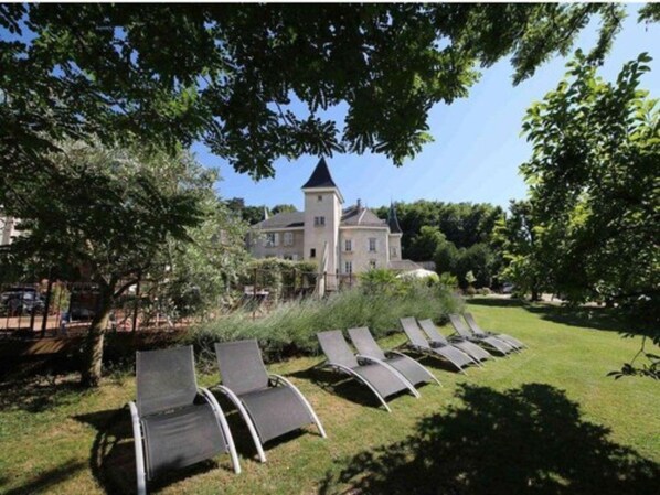 A large building with a tower, surrounded by a well-maintained lawn and several lounge chairs. - Château & Spa de la Commanderie (Eybens)
