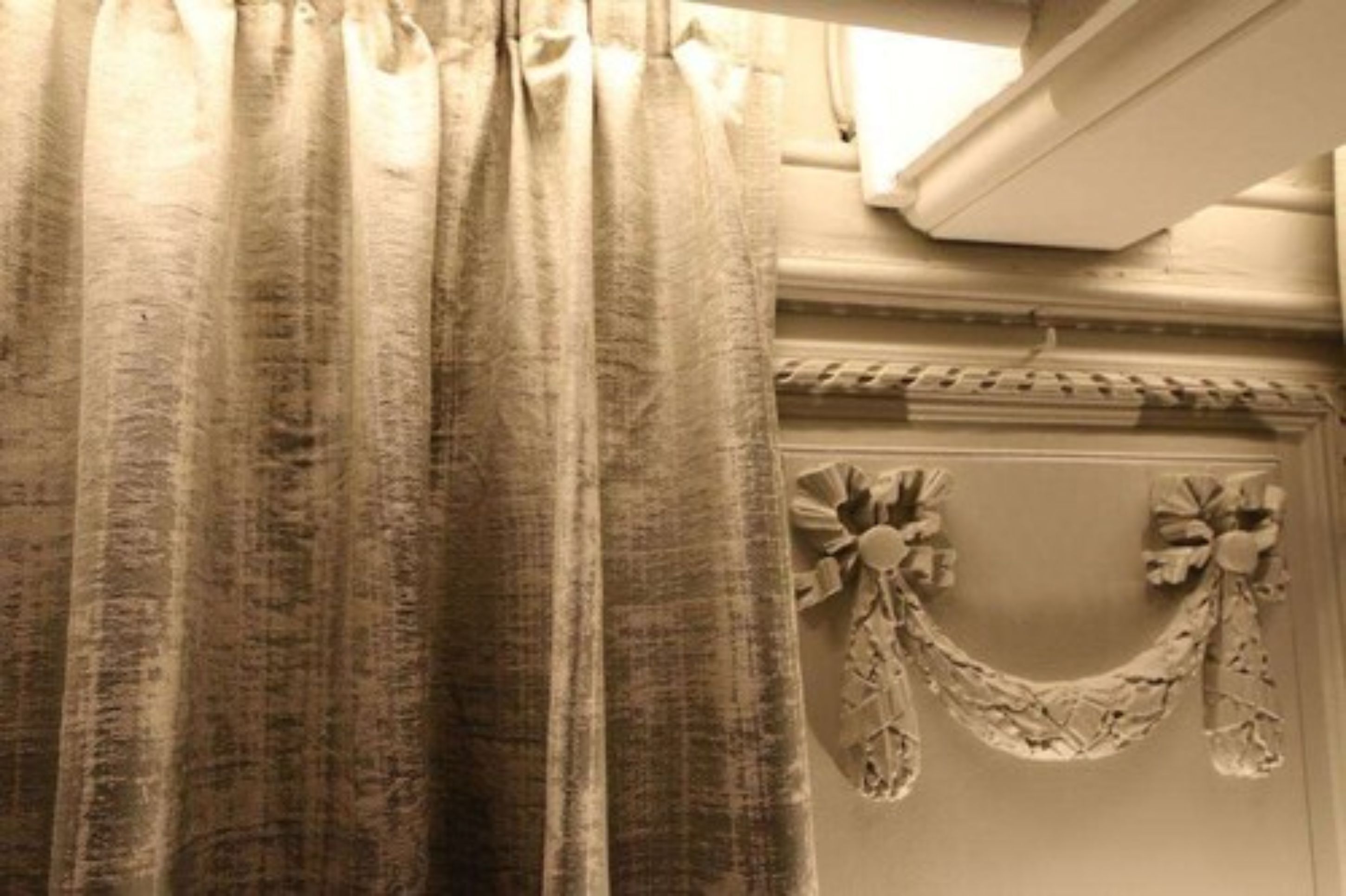 A bathroom with a beige curtain, a decorative garland with flowers, and a window with a white frame.