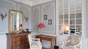 Una habitación con un espejo grande, un escritorio con lámpara, dos sillas, un aparador y una ventana que ofrece vista a un dormitorio.