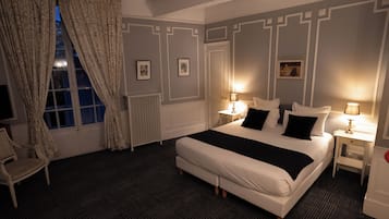 Une chambre d’hôtel bien aménagée, avec un grand lit, deux tables de chevet avec des lampes, une chaise et une fenêtre avec des rideaux.