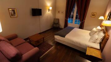 A hotel room with a bed, a sofa, a chair, a small table, and a TV mounted on the wall.