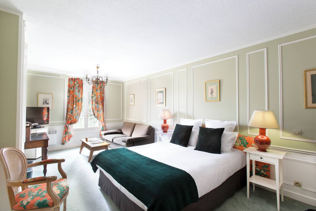 A hotel room with a bed, a desk, a chair, a lamp, and a television.