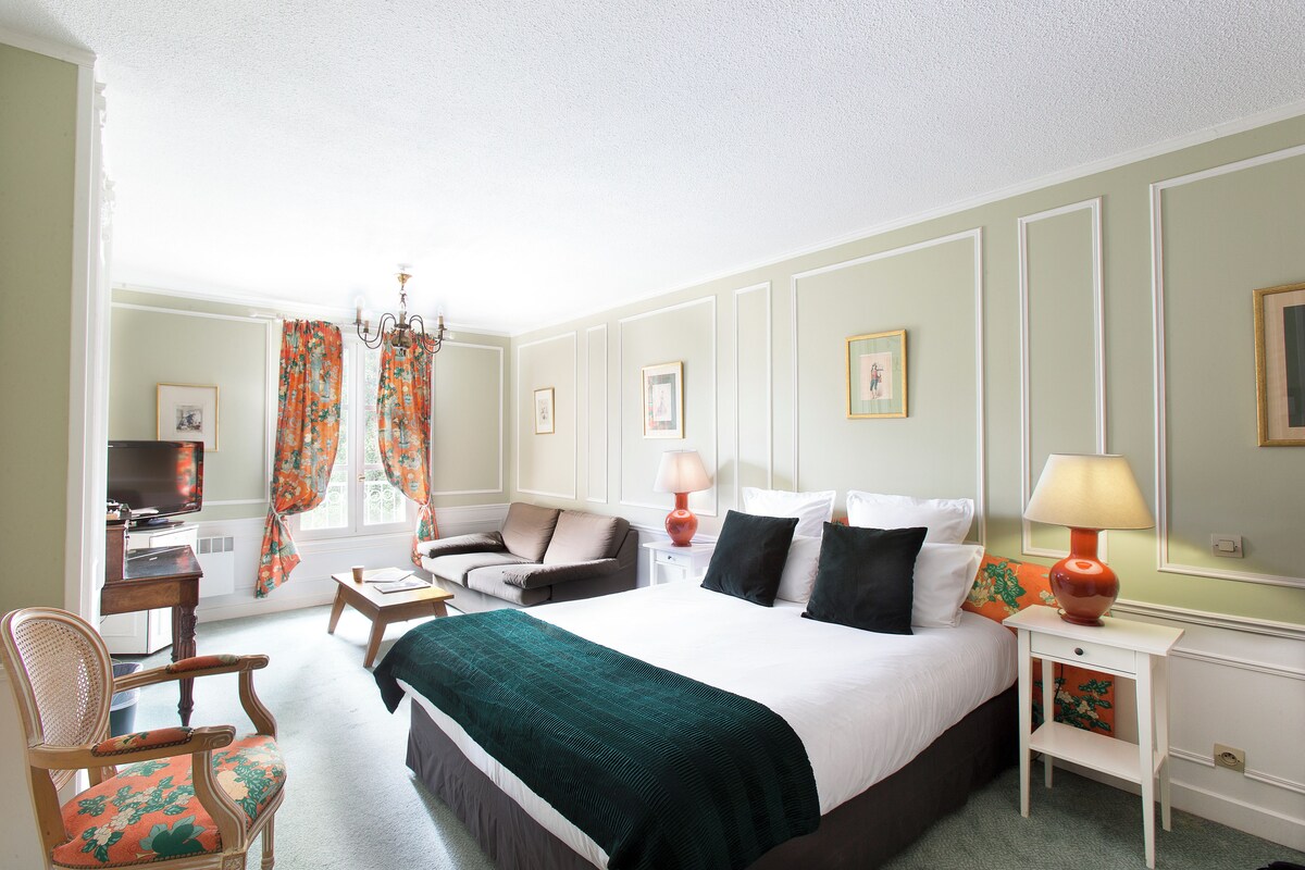 A hotel room with a bed, a desk, a chair, a lamp, and a television.