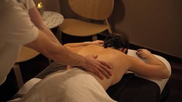 A massage therapy session in a room with a wooden chair and a small round table with a candle.