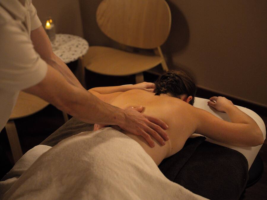 Une séance de massage dans une pièce où se trouvent une chaise en bois et une petite table ronde avec une bougie.