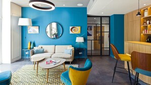 Una sala de estar moderna con una pared azul de acento, un espejo redondo, un sofá, una mesa de centro y una zona de bar con taburetes.