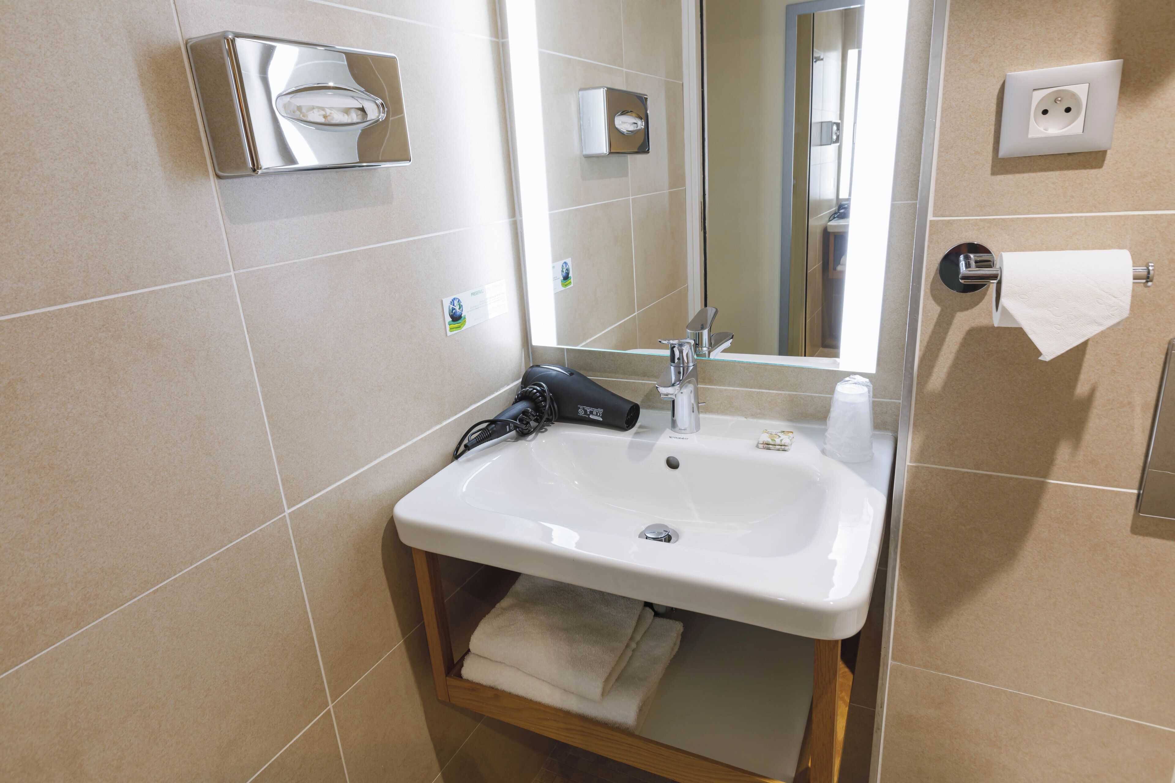 A bathroom with a sink, mirror, towel dispenser, and a towel rack.