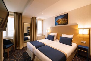 Camera d'albergo con due letti, televisione, scrivania e finestra con tende.
