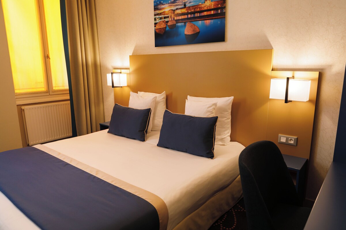 Una habitación de hotel con una cama, dos lámparas de noche, una mesita de noche y un cuadro en la pared.