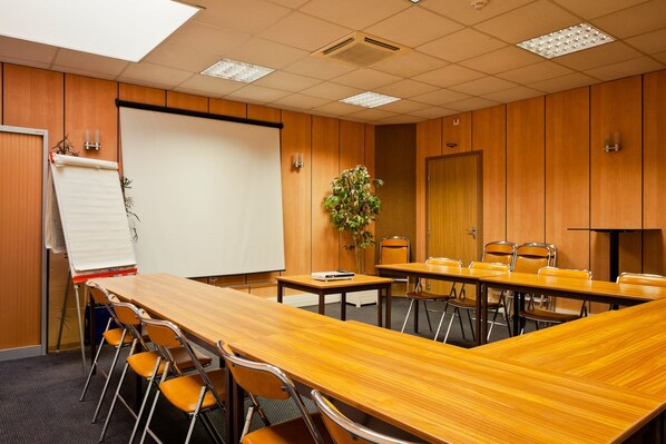 Una sala de conferencias con una larga mesa de madera, múltiples sillas, una pizarra y una pantalla para proyector.