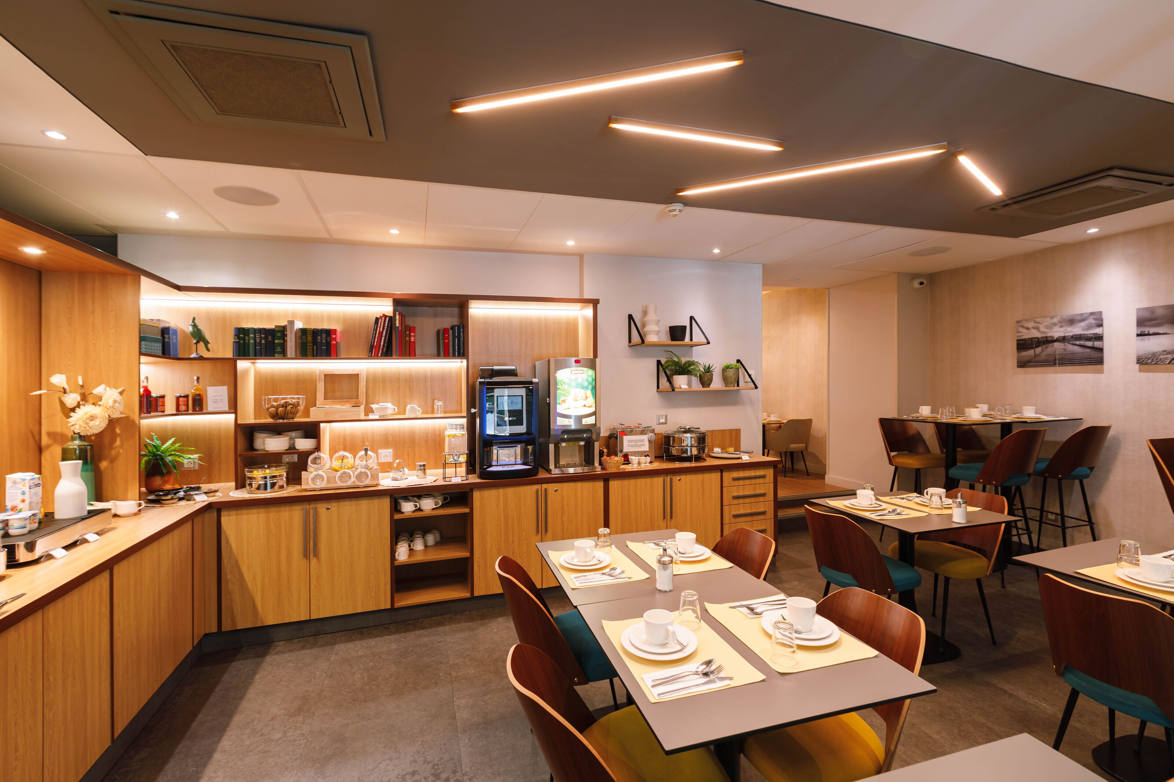 Un espace repas moderne, doté de meubles en bois, d’une machine à café et de diverses étagères où sont disposés des livres et des objets décoratifs.