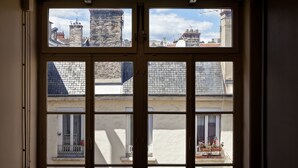 Una ventana con vistas a edificios y un balcón lleno de flores.