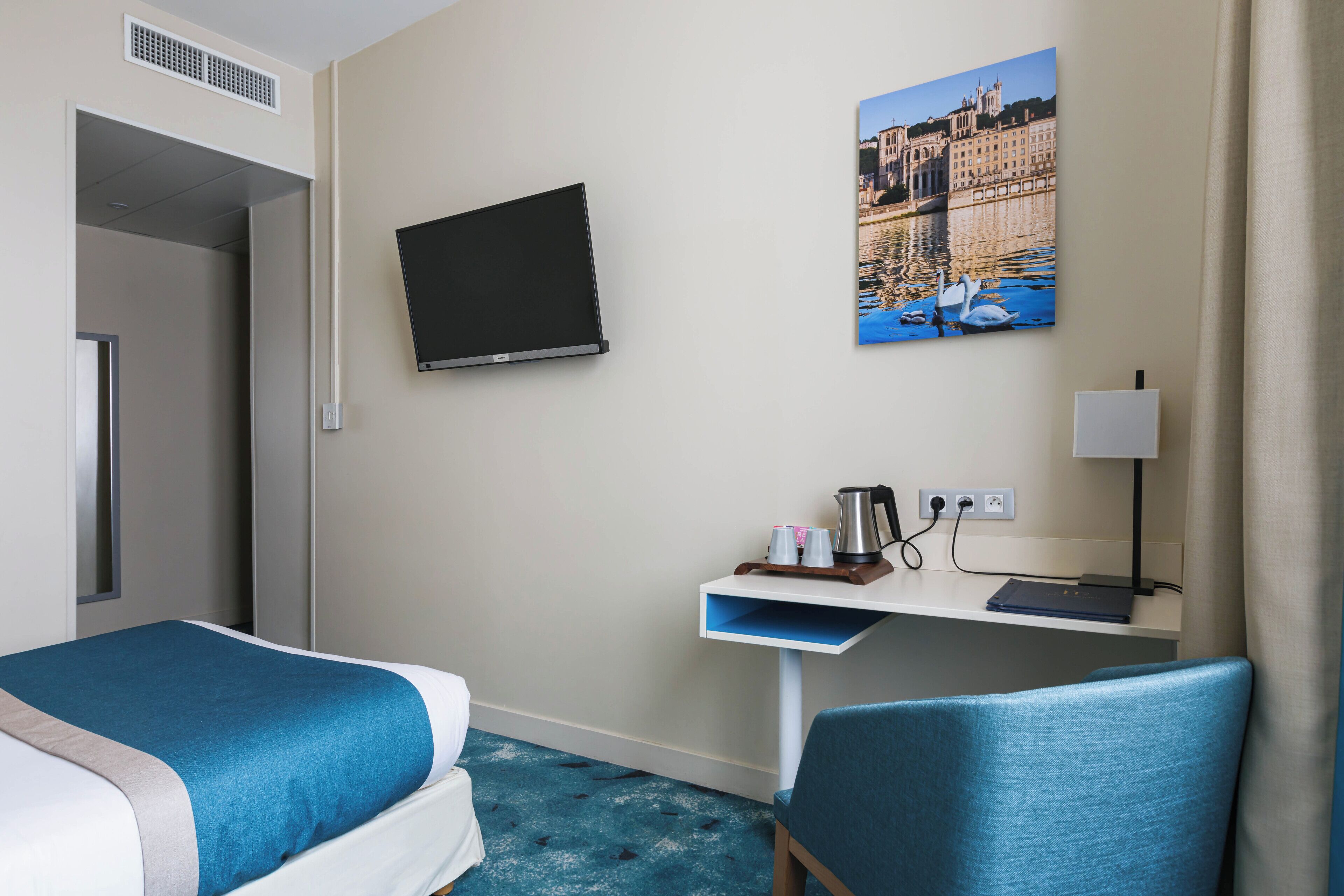 A hotel room with two beds, a desk with a laptop, a flat-screen TV, a painting of a river scene, and a chair.