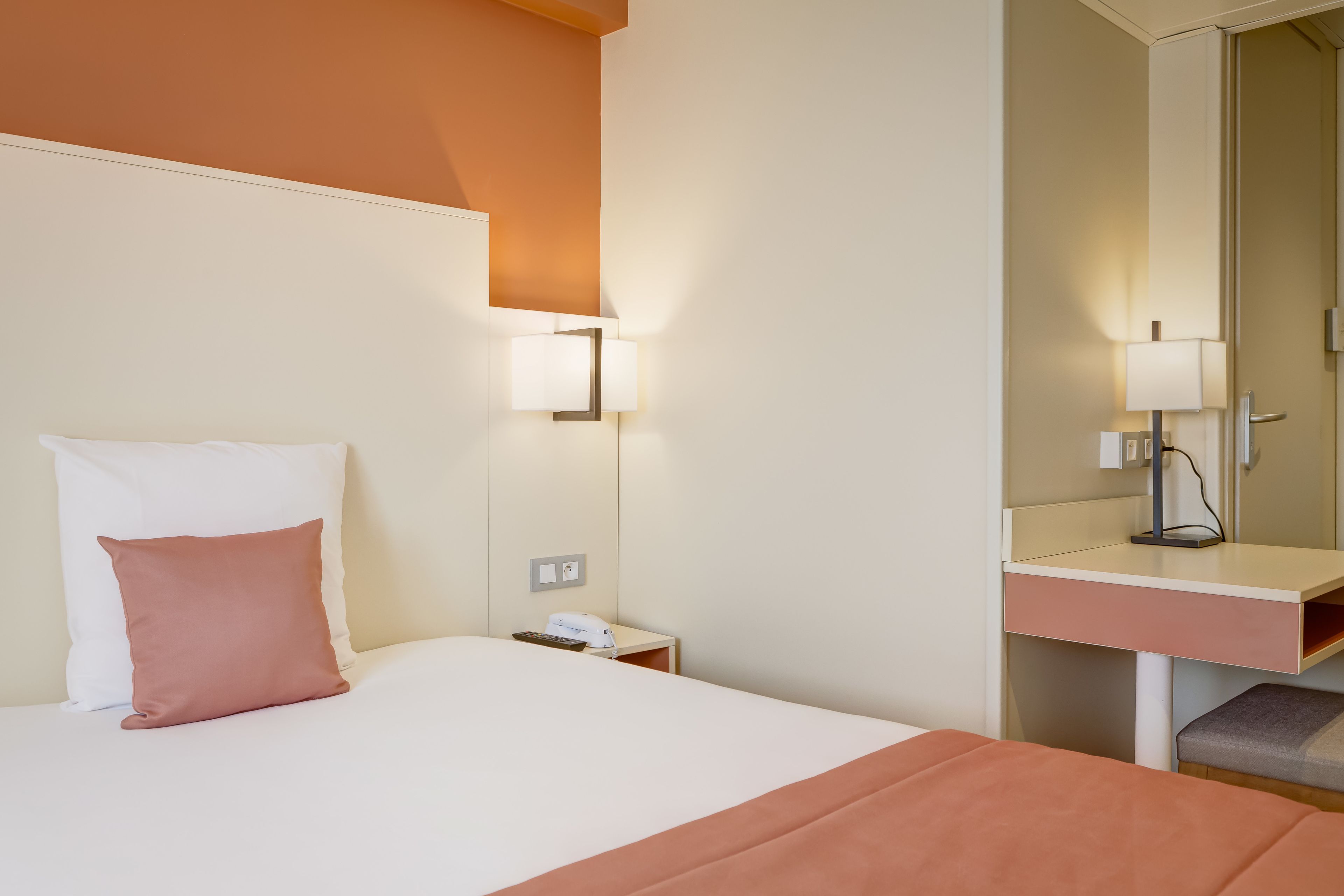 Een hotelkamer met een bed, nachtkastje, bureau en spiegel.