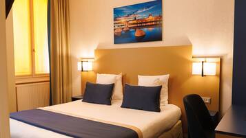 A hotel room with a large bed, two bedside lamps, a desk, and a chair.