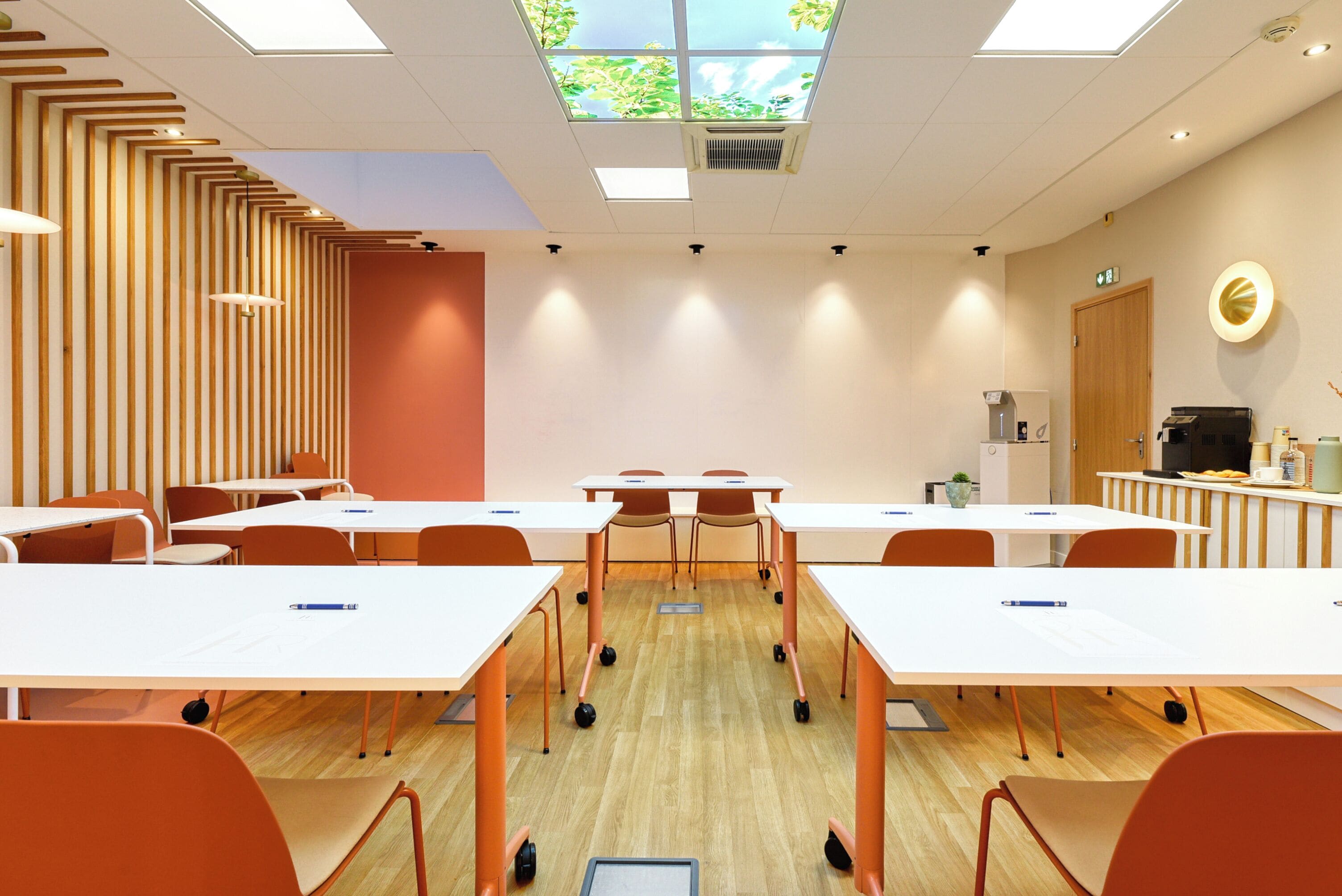 A modern conference room with white tables, orange chairs, and a wooden accent wall.