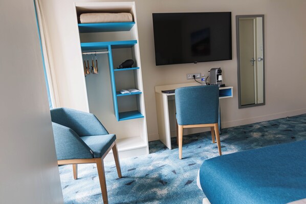 A hotel room with a bed, a desk with a chair, a TV, and a wardrobe with shelves. - Hôtel des Remparts Lyon Perrache (Lyon)