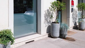 Un hotel llamado "EL DES REMPARTS" con amplios ventanales de vidrio, plantas en macetas afuera y un cartel que indica que se trata de un hotel.