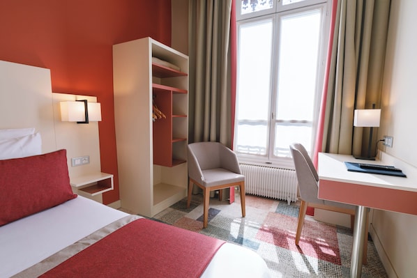 A hotel room with a bed, a desk, a chair, a wardrobe, and a window with curtains. - Hôtel des Remparts Lyon Perrache (Lyon)
