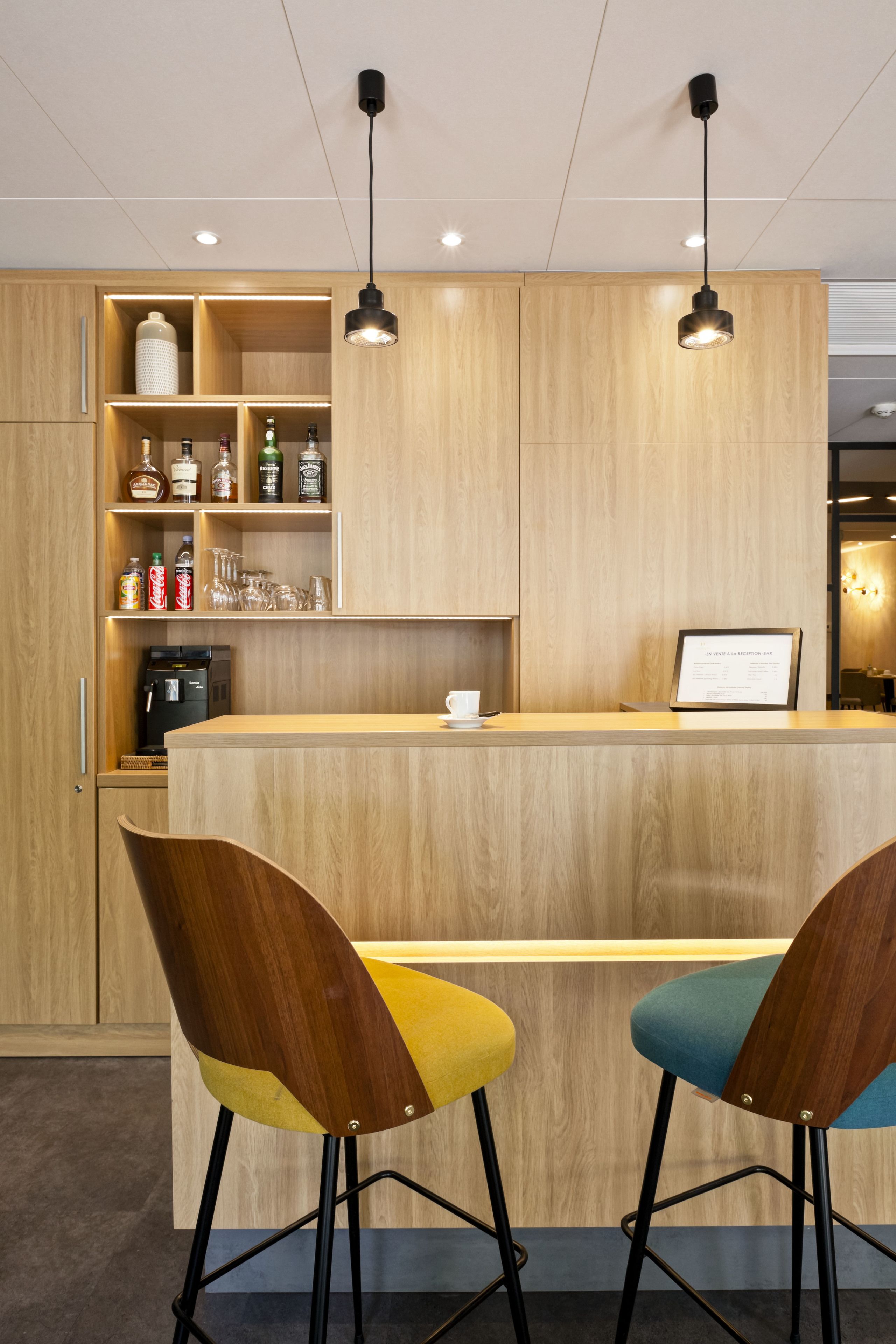 Una cocina moderna con armarios de madera, una cafetera integrada y dos taburetes de bar coloridos.