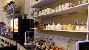 A buffet area with shelves of white dishes, a counter with food items, and a television displaying a menu. - Regina Hotel (Avignon)