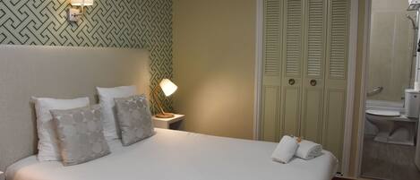 A neatly made bed with pillows, a bedside lamp, and a towel on the bed.
