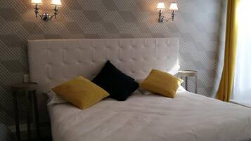 Een hotelkamer met een gestoffeerd hoofdeinde, twee bedlampen en een bed met wit beddengoed en twee kussens.