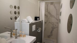 A modern bathroom with a white sink, mirror, and toilet. There are toiletries on the counter and a shower curtain with a marble pattern. - Regina Hotel (Avignon)