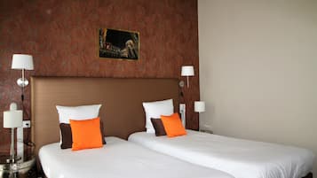A hotel room with two beds, white bedding, and orange pillows. There are two bedside lamps and a picture on the wall.
