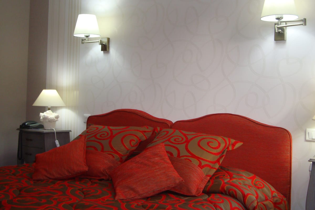 Une chambre d’hôtel comprenant un lit, deux lampes fixées au mur, une table de chevet avec une lampe et un téléphone.