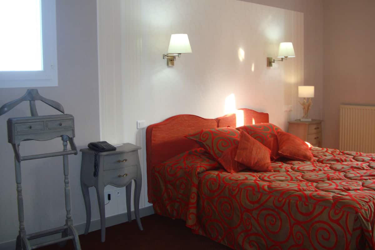 Une chambre à coucher avec un lit, deux lampes de chevet, une table de chevet, une chaise et une fenêtre.