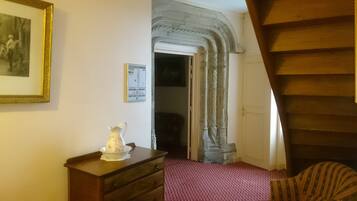 A room with a wooden staircase, a red patterned carpet, a wooden dresser, a white pitcher, and a framed picture on the wall.